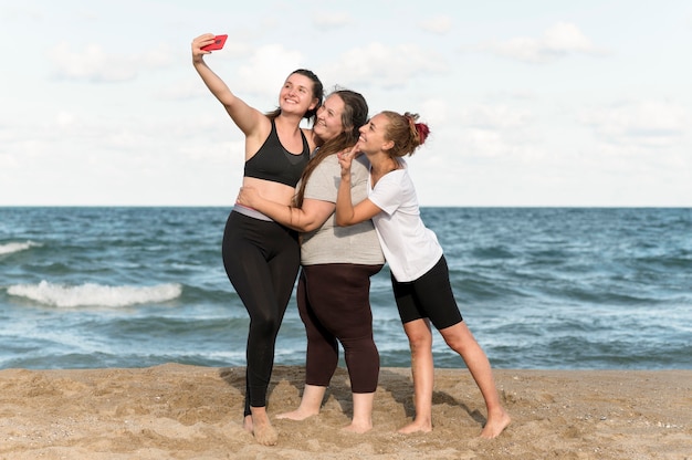 Donne del colpo pieno che prendono selfie in riva al mare