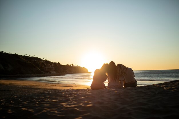 Donne del colpo pieno che si siedono sulla spiaggia al tramonto