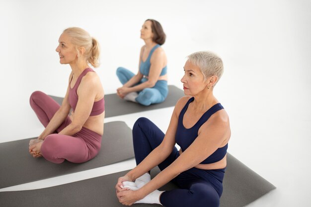 Donne del colpo pieno che si siedono sulla stuoia di yoga