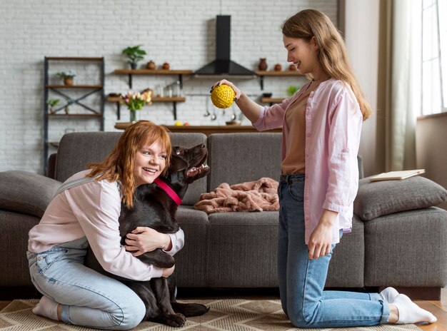 Donne del colpo pieno e cane che giocano con la palla