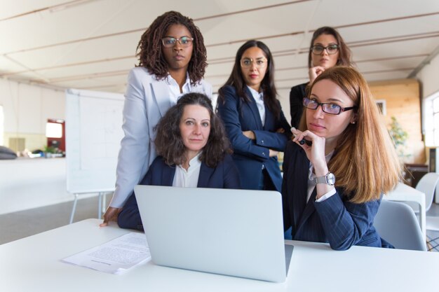 Donne di affari che per mezzo del computer portatile e esaminando macchina fotografica