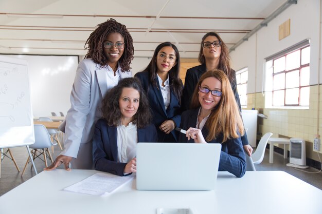 Donne di affari che per mezzo del computer portatile e sorridendo alla macchina fotografica