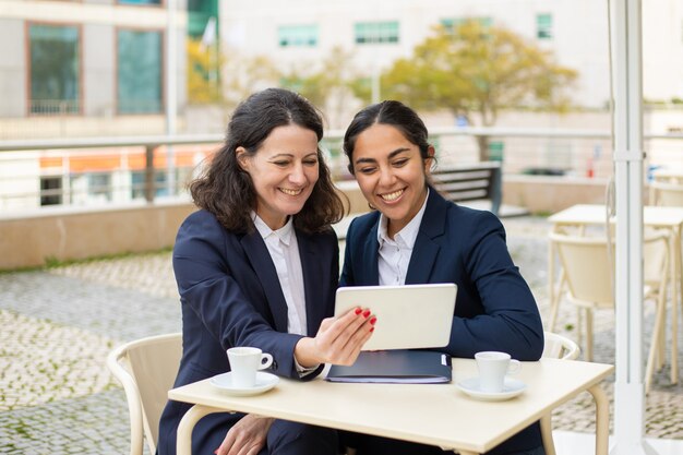 Donne di affari contente con il pc della compressa in caffè all'aperto