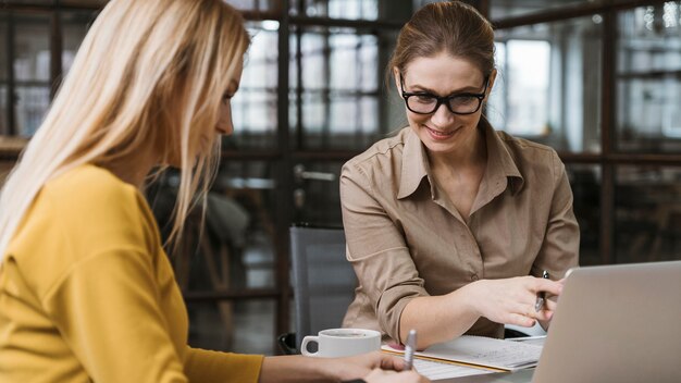 Donne di affari di smiley che lavorano con il computer portatile allo scrittorio all'interno