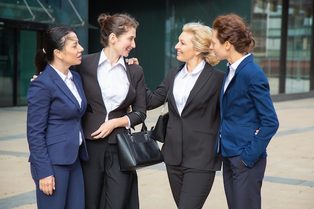 Donne di affari felici che celebrano il successo della squadra, stando all'aperto, abbracciando e parlando. Supporto del team e concetto di congratulazioni