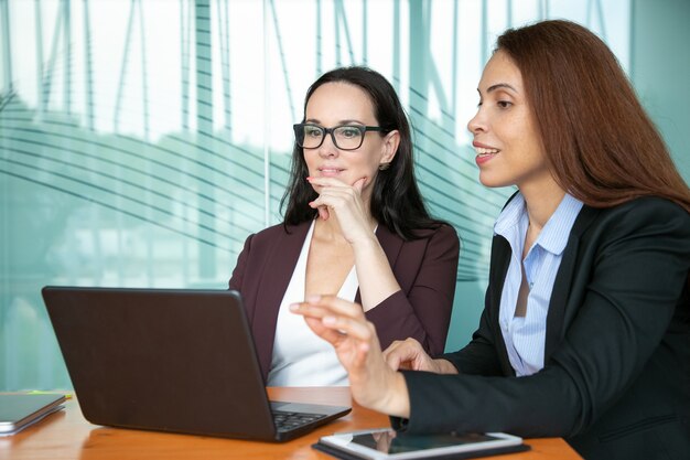 Donne di affari sorridenti concentrate che esaminano l'esposizione aperta del computer portatile