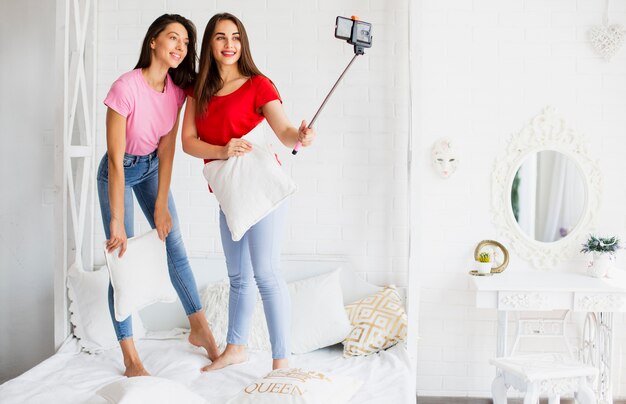 Donne di smiley a letto con il cuscino che cattura foto