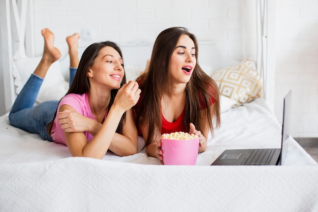 Donne di smiley che guardano al computer portatile e che mangiano popcorn