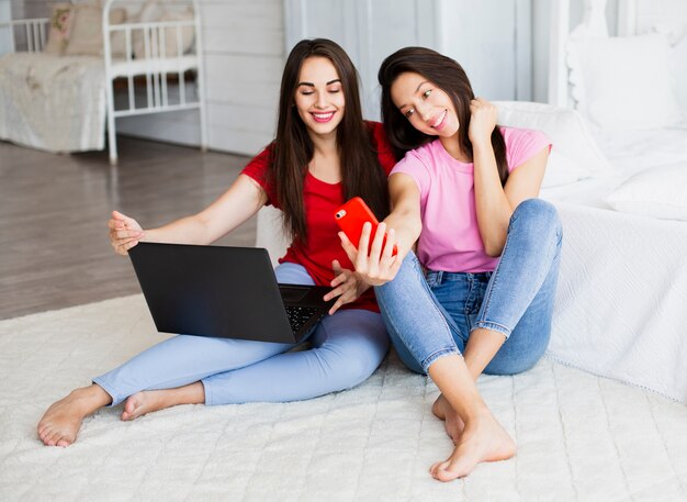 Donne di smiley che si siedono sul pavimento e che prendono selfie