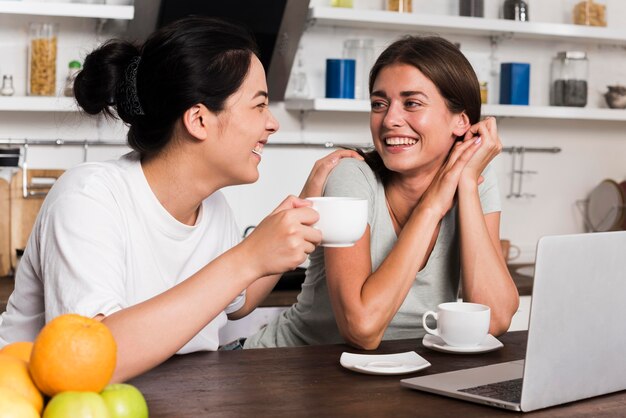 Donne di smiley in cucina con laptop e caffè