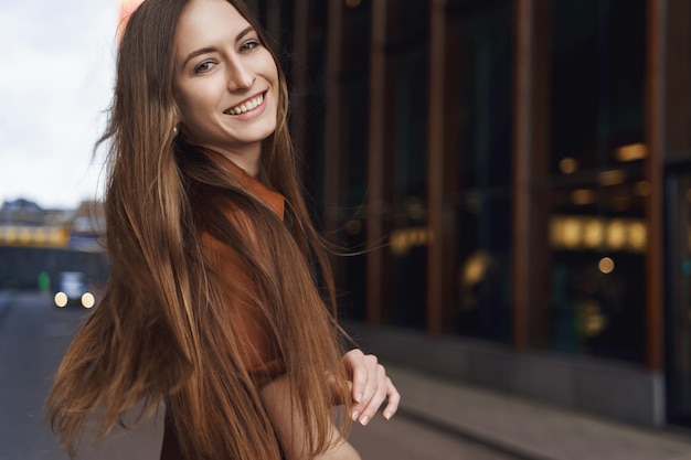 Donne e concetto di business Felice romantica giovane donna caucasica in abito in finta pelle marrone girarsi dietro per sorridere alla telecamera vento che soffia ai capelli signora sentirsi spensierata e gioiosa