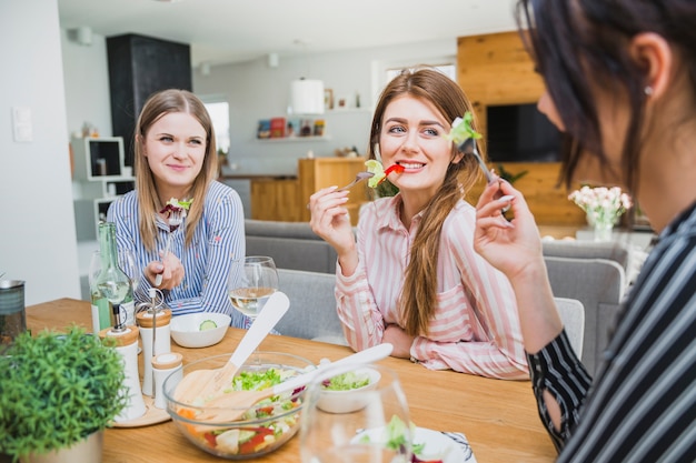 Donne graziose che mangiano alla tavola e che sorridono