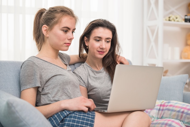 Donne lesbiche che si siedono sul sofà facendo uso del computer portatile a casa