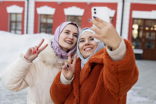 Donne musulmane che si fanno un selfie con uno smartphone e mostrano il segno della pace mentre sono in vacanza