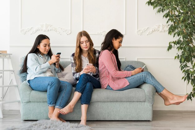 Donne sedute sul divano e caricate nei telefoni