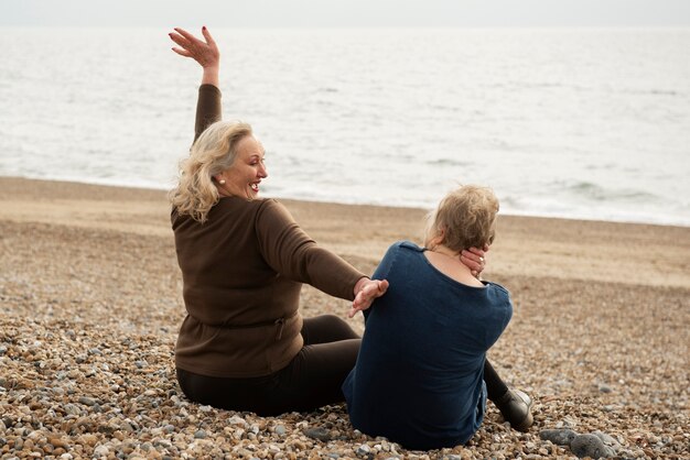 Donne senior del colpo pieno che si siedono sulla spiaggia