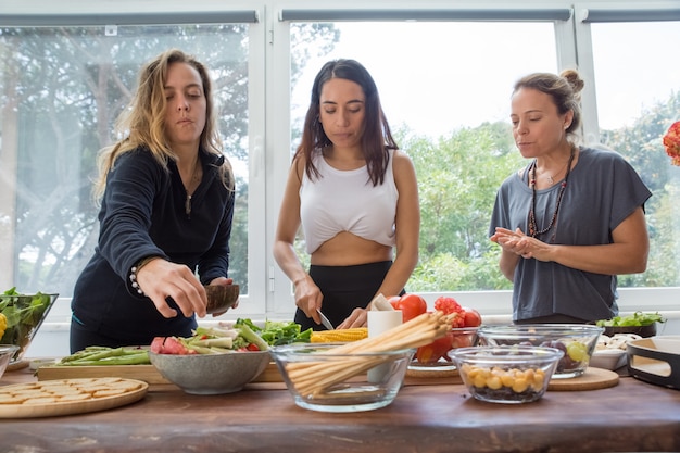 Donne seri che cucinano le verdure al tavolo da cucina