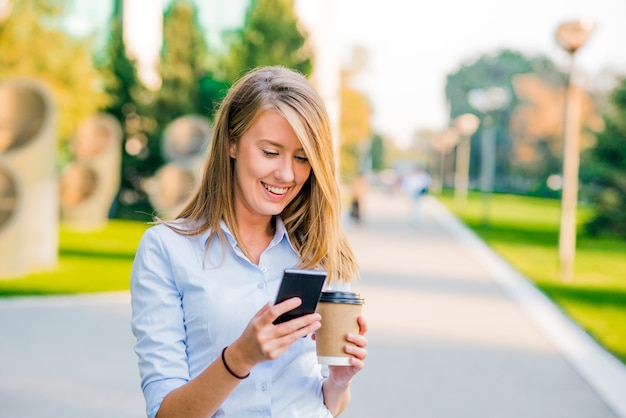 Donne sicure che leggono informazioni sulle notizie di finanza mentre si cammina nel corridoio dell&#39;azienda durante il break di lavoro, la donna d&#39;affari di successo che scrive il messaggio di testo il suo cliente mentre va con il segretario di ufficio