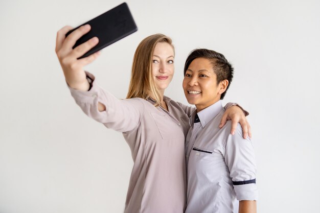 Donne sorridenti che abbracciano e prendendo selfie foto