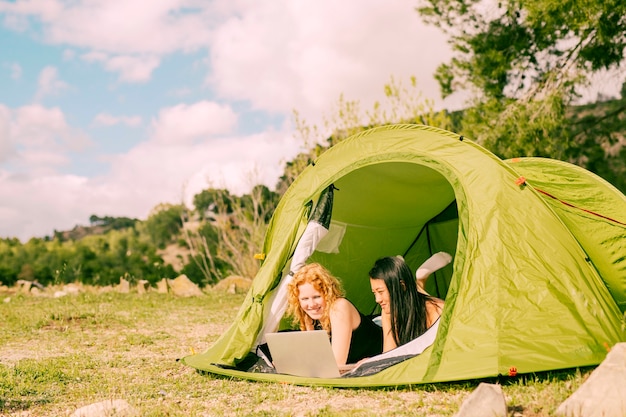 Donne sorridenti che si trovano in tenda con il computer portatile