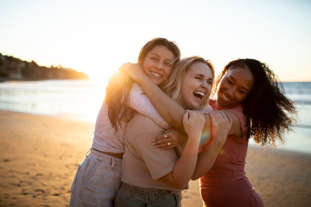 Donne sorridenti del colpo medio che si abbracciano in spiaggia