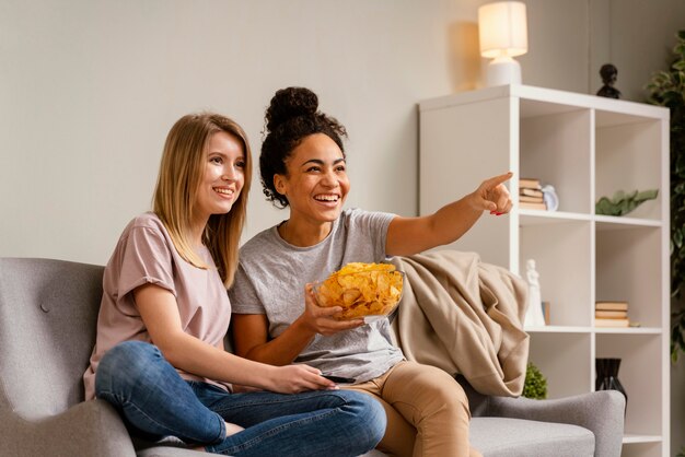 Donne sul divano a guardare la tv e mangiare patatine