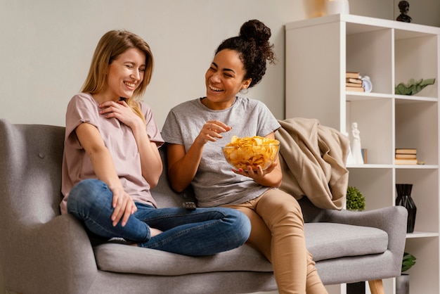 Donne sul divano a guardare la tv e mangiare patatine