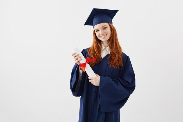 Dottorando femminile della testarossa con sorridere del diploma. Copyspace.