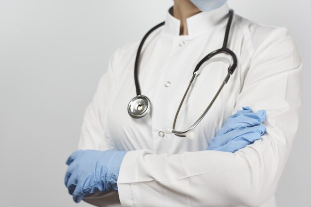 Dottore in uniforme bianca con stetoscopio in piedi con le braccia incrociate