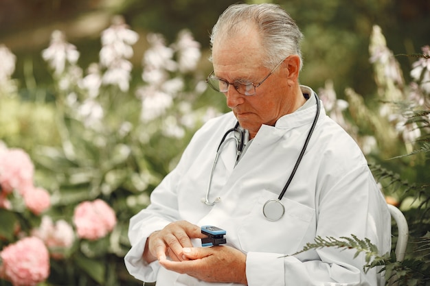 Dottore in uniforme bianca. Il vecchio uomo seduto in un parco estivo. Anziano con lo stetoscopio. L'uomo misura il polso sul dito.