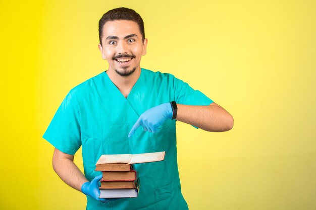 Dottore in uniforme e maschera a mano in piedi e indicando i suoi libri.