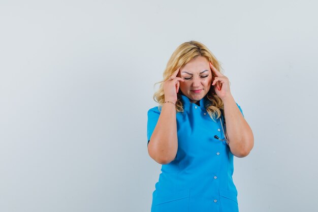 Dottoressa che massaggia le tempie in uniforme blu e cerca spazio stressante per il testo