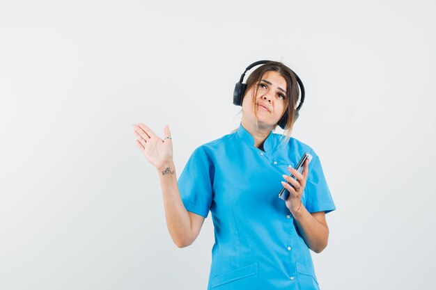 Dottoressa che si gode la musica con le cuffie, tenendo il telefono cellulare in uniforme blu blue