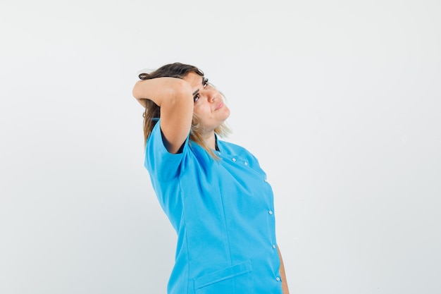 Dottoressa in uniforme blu che guarda in alto con la mano sui capelli e sembra elegante