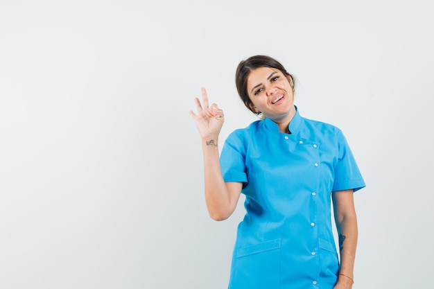 Dottoressa in uniforme blu che mostra gesto ok e sembra allegra