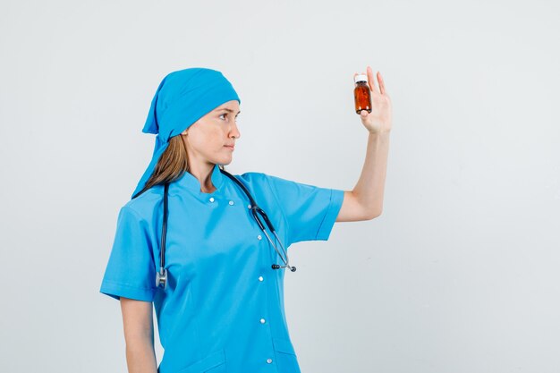 Dottoressa in uniforme blu che tiene la bottiglia del farmaco e che sembra seria