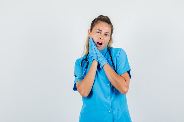 Dottoressa in uniforme blu, guanti che soffrono di mal di denti e che sembra infastidita