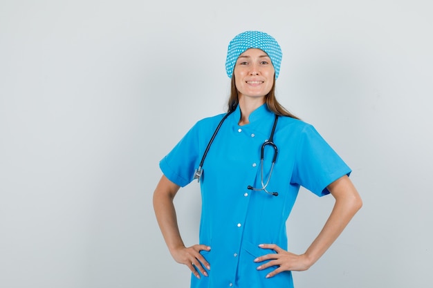 Dottoressa in uniforme blu in piedi con le mani sulla vita e guardando fiducioso