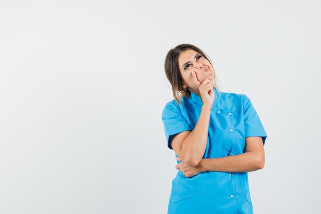 Dottoressa in uniforme blu in piedi in posa pensante e dall'aspetto irresoluto