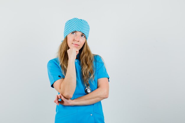 Dottoressa in uniforme blu in piedi nella posa di pensiero e in cerca di speranza