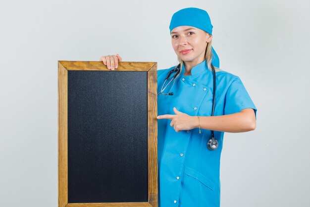 Dottoressa in uniforme blu puntare il dito alla lavagna e guardando positivo