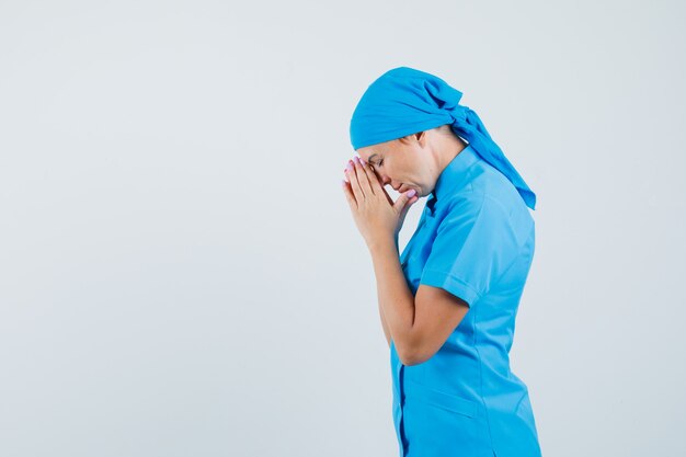 Dottoressa in uniforme blu tenendosi per mano nel gesto di preghiera e guardando speranzoso.
