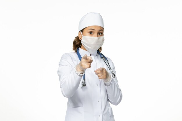 Dottoressa vista frontale in tuta medica bianca e con maschera a causa di coronavirus su malattia da virus della parete bianca leggera pandemia covid