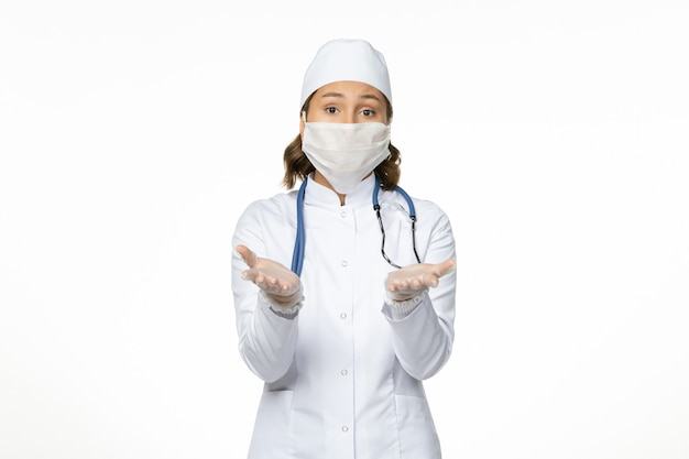 Dottoressa vista frontale in tuta medica bianca e con maschera a causa di coronavirus su virus del muro bianco malattia pandemica covid