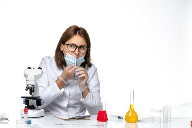 Dottoressa vista frontale in tuta medica con maschera a causa di covid lavorando con soluzioni sulla scrivania bianca