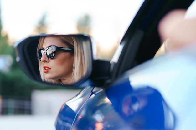 Driver della giovane donna che guarda nello specchietto retrovisore dell'auto, assicurandosi che la linea sia libera prima di girare.