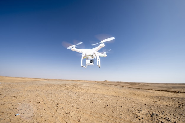 Drone bianco che sorvola un'area desertica arida contro un cielo blu