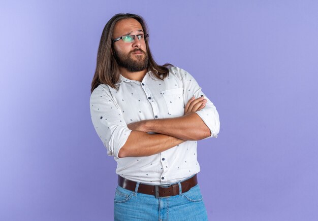 Dubbioso bell'uomo adulto con gli occhiali in piedi con la postura chiusa guardando il lato isolato sul muro viola con spazio copia