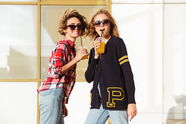 Due adolescenti felici in occhiali da sole che bevono il succo di arancia