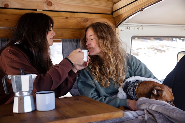 Due amanti femminili che bevono caffè e trascorrono del tempo con il loro boxer in un camper durante il viaggio invernale